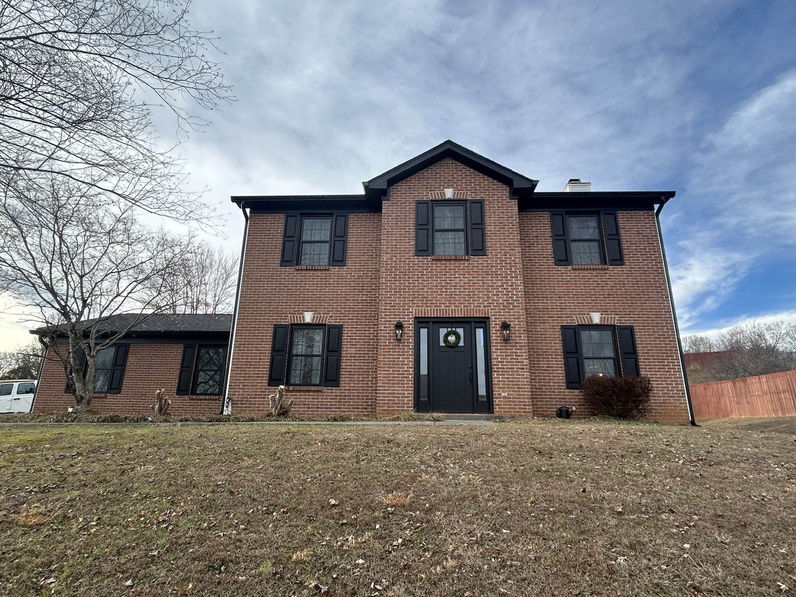 After: Same brick home with new roof, new shutters, new front door, and refreshed trim